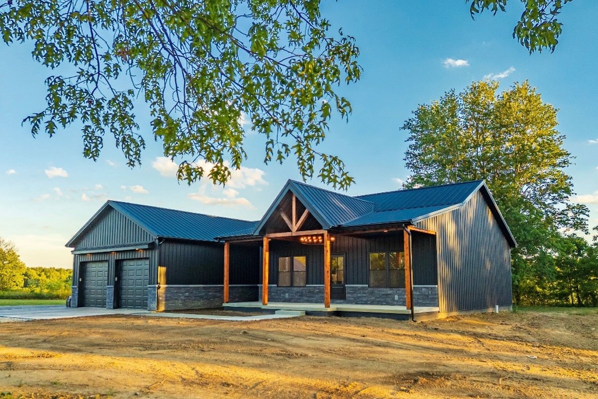 The same Legacy Developments custom home finished and move-in ready — black board-and-batten with metal roof, stone, and timber porch