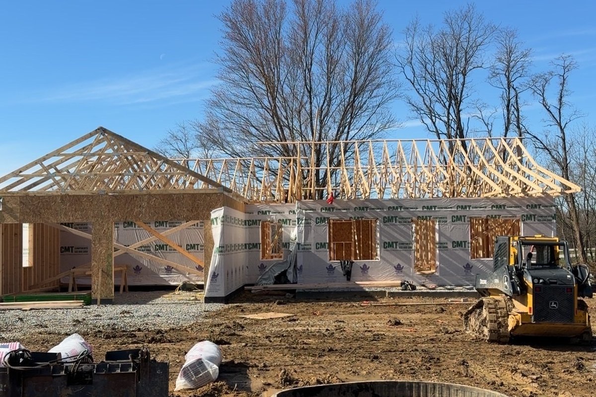 Legacy Developments custom home during construction — framing, roof trusses, and house wrap